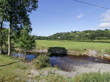 A river with trees and a field at Plas Glan Yr Afon in Llangernyw