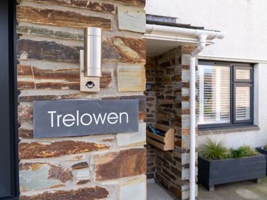 A stone wall with a sign reading Trelowen and a light fixture next to a window with white shutters and a planter box at Trelowen St Issey near Padstow