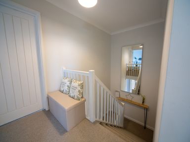 A staircase landing with a bench with cushions a mirror and a small table at Trelowen in St Issey near Padstow