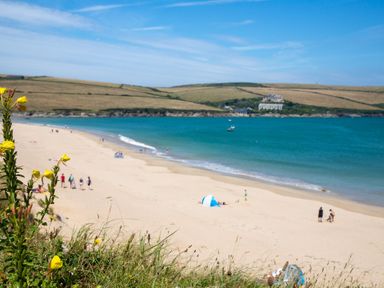 A beach scene with sand, water, and people at Trelowen in St Issey near Padstow
