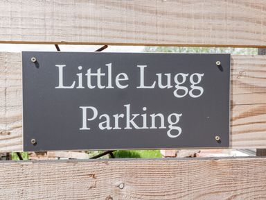 A black sign with white text reading Little Lugg Parking attached to a wooden fence at Little Lugg in Cross Keys near Hereford