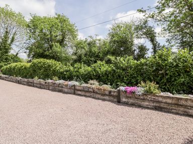 A gravel parking area with a wooden planter containing flowers and green hedges in the background at Little Lugg Cross Keys near Hereford