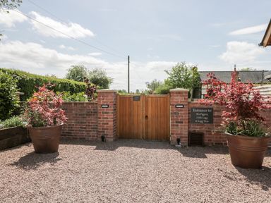 A gravel courtyard with two large potted plants and a wooden gate in a brick wall at Little Lugg in Cross Keys near Hereford