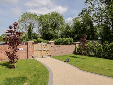 A driveway leading to wooden gates set in a brick wall with grass and small trees on both sides at Little Lugg in Cross Keys near Hereford