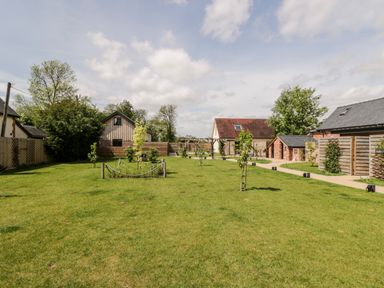 An outdoor garden area with young trees on a lawn and small buildings in the background at Little Lugg in Cross Keys near Hereford