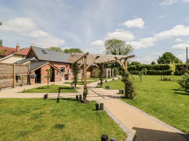 A garden with a wooden pergola on paved pathways next to a brick building at Little Lugg in Cross Keys near Hereford