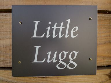 A black sign with white text reading Little Lugg mounted on a wooden surface at Little Lugg in Cross Keys near Hereford