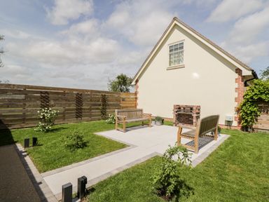 A garden with two wooden benches a brick barbecue on a paved area grass and a wooden fence at Little Lugg in Cross Keys near Hereford
