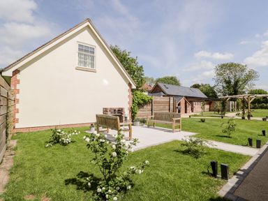 A garden area with two wooden benches on a paved section surrounded by grass and small flowering bushes at Little Lugg Cross Keys near Hereford
