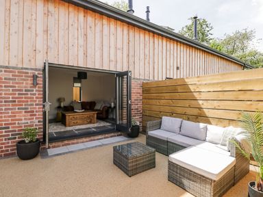 An outdoor patio area with gray cushioned wicker seating and a glass table next to a building with wooden and brick walls at Little Lugg in Cross Keys near Hereford