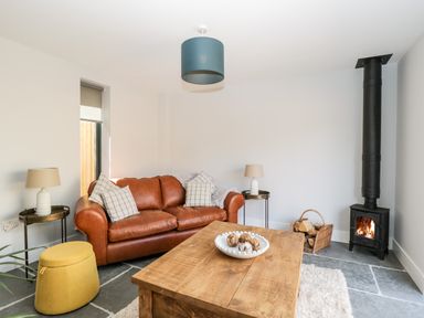 A living room with a brown leather sofa and a wood burning stove at Little Lugg in Cross Keys near Hereford