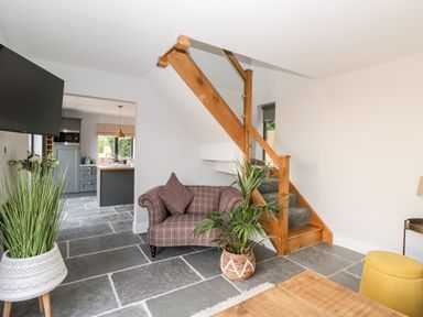 A sitting area with a plaid armchair and plants near wooden stairs with glass panels at Little Lugg Cross Keys near Hereford