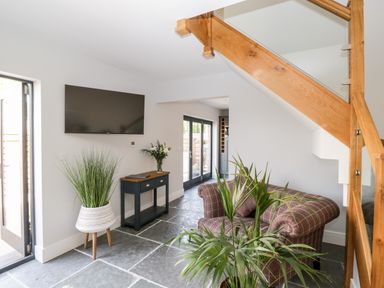A living room with a mounted television a plaid armchair plants a small console table and wooden staircase at Little Lugg in Cross Keys near Hereford
