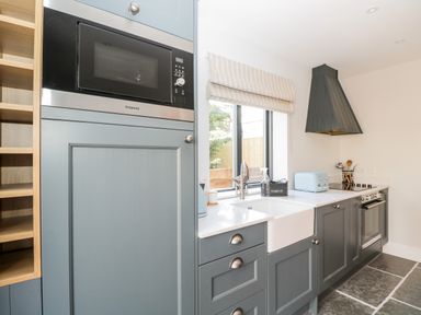 A kitchen with blue cabinets a microwave an oven a sink and a window at Little Lugg in Cross Keys near Hereford