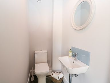 A small bathroom with a toilet a wall-mounted sink a round mirror and a basket with toilet paper at Little Lugg in Cross Keys near Hereford