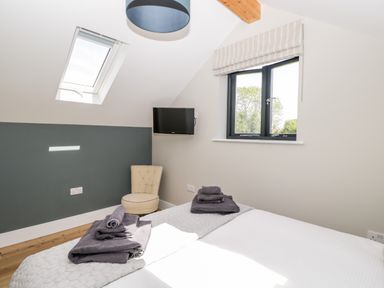 A bedroom with two beds with gray towels on them a small upholstered chair a wall-mounted television a skylight and a window with beige blinds at Little Lugg in Cross Keys near Hereford