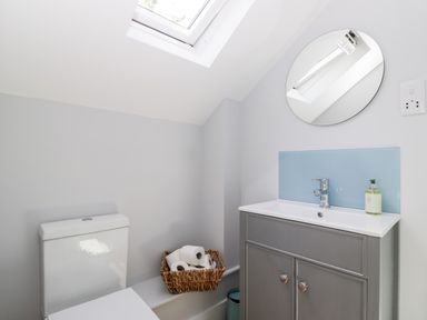 A bathroom with a toilet, basket with toilet paper rolls, sink with cabinet, round mirror, and skylight at Little Lugg in Cross Keys near Hereford