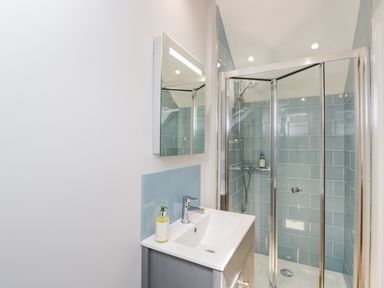 A bathroom with a sink and mirror next to a glass-enclosed shower with blue tiles at Little Lugg in Cross Keys near Hereford
