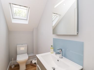 A bathroom with a toilet, sink with a chrome faucet, a mirror, a window, and a basket with toilet paper at Little Lugg in Cross Keys near Hereford