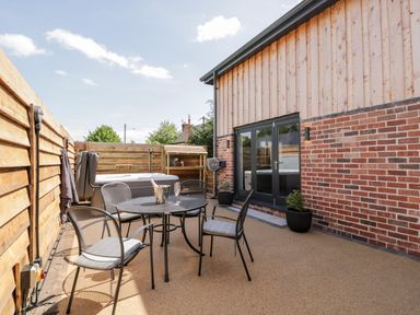 An outdoor patio with a round metal table and four chairs a hot tub a wooden fence and a brick and wood building at Little Lugg in Cross Keys near Hereford