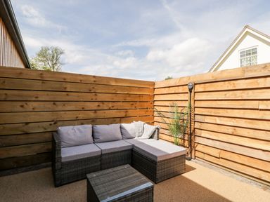 An outdoor seating area with a wicker sofa and coffee table surrounded by wooden fencing at Little Lugg in Cross Keys near Hereford