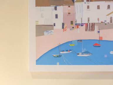 A framed abstract painting of boats in water with buildings in the background on a light wall