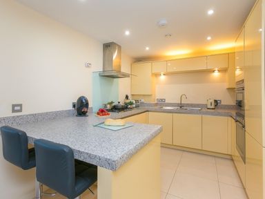 A kitchen with yellow cabinets grey countertops a sink stove kettle and two black chairs at Golden Sands in Carbis Bay
