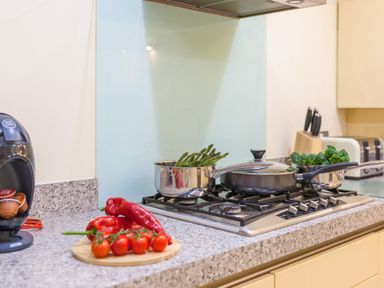 A kitchen countertop with red peppers and cherry tomatoes on a cutting board next to a stove with pots containing asparagus and broccoli at Golden Sands in Carbis Bay