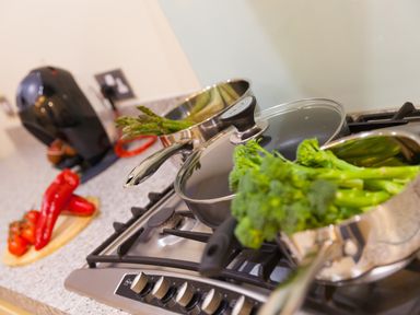 A kitchen stove with pots containing asparagus and broccoli and a countertop with red peppers and tomatoes at Golden Sands in Carbis Bay