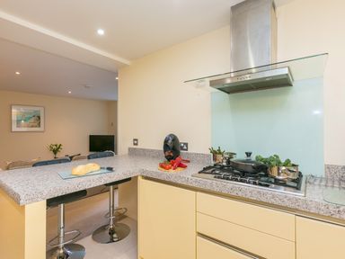 A kitchen with a countertop stove pots of vegetables and bar stools at Golden Sands in Carbis Bay