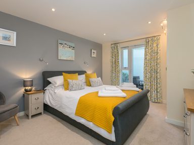 A bedroom with a double bed with yellow throw and pillows bedside tables and a chair at Golden Sands in Carbis Bay