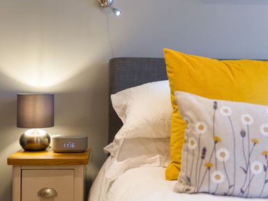 A bedside table with a lamp and digital clock next to a bed with white and yellow pillows in a bedroom at Golden Sands in Carbis Bay