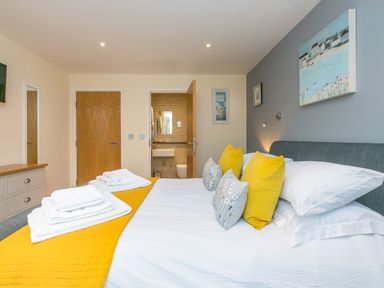 A bedroom with a bed with yellow and patterned pillows a dresser and an open door showing a bathroom at Golden Sands in Carbis Bay