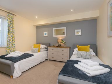 A bedroom with two single beds a chest of drawers and patterned curtains at Golden Sands in Carbis Bay