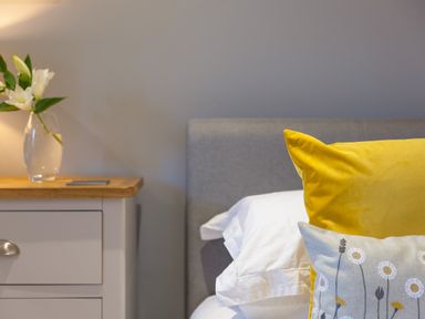 A bedside table with a vase of flowers next to a bed with a yellow and floral pillow at Golden Sands in Carbis Bay