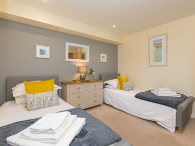 A bedroom with two single beds a chest of drawers with a lamp and flowers and framed pictures on the walls at Golden Sands in Carbis Bay