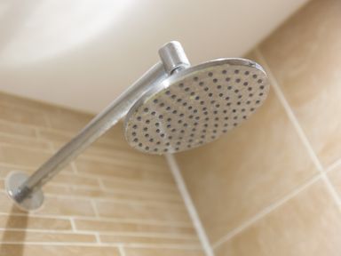 A close up of a circular showerhead with water holes attached to a metal arm in a tiled bathroom at Golden Sands in Carbis Bay