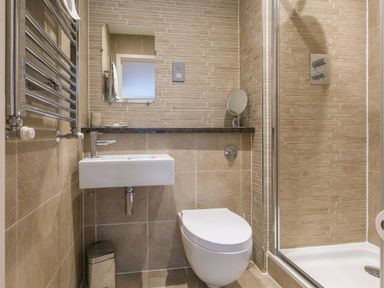 A small bathroom with a wall-mounted sink a toilet a glass shower enclosure and a mirror on a tiled wall at Golden Sands in Carbis Bay