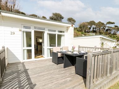 A wooden deck with outdoor dining table and chairs outside a white house with large windows at Seas The Day in Ventnor
