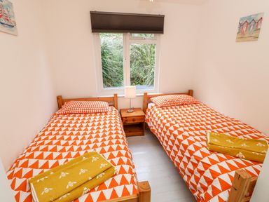 A bedroom with two single beds with orange and white patterned bedding and a small wooden nightstand with a lamp by the window at Seas The Day Ventnor