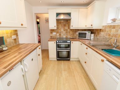 A kitchen with wooden countertops white cabinets an oven a microwave a dish rack and a sink at Seas The Day in Ventnor