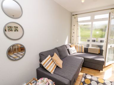 A living room with a gray sofa and striped cushions next to a window with curtains and a set of three round mirrors on the wall at Seas The Day in Ventnor
