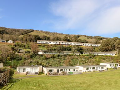Single story houses with fenced yards on a grassy hillside with hills and trees in the background at Seas The Day in Ventnor