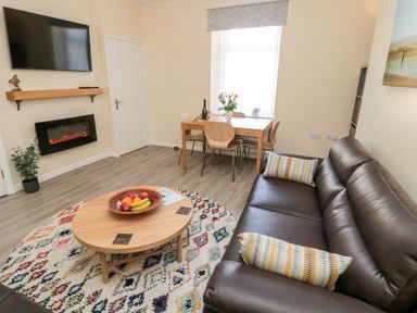 A living room with a brown leather sofa a round rug and a wooden coffee table at Stones Throw in Amble