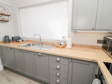 A kitchen with grey cabinets wooden countertop stainless steel sink and appliances at Stone's Throw in Amble