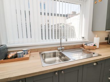 A kitchen countertop with a stainless steel sink a wooden tray with two mugs and a toaster and a basket with dishcloths at Stones Throw in Amble