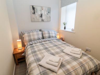 A bedroom with a double bed plaque and bedside tables with lamps at Stone's Throw in Amble