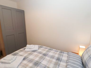 A bedroom with a bed with plaid bedding folded towels on the bed a bedside lamp and a gray wardrobe at Stones Throw in Amble