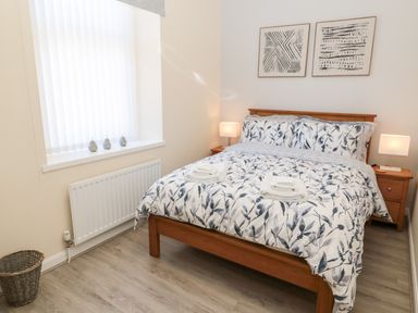 A bedroom with a bed with patterned bedding two bedside tables with lamps and framed artwork on wall at Stone's Throw in Amble