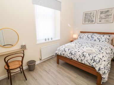 A bedroom with a bed and patterned bedding a chair a round mirror and two framed pictures on the wall at Stone's Throw in Amble